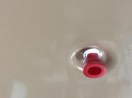 Breezaire bottom drain fitting with red cap installed on beige wine cellar cooling unit panel.