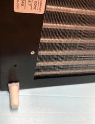 Breezaire rear drain fitting modified on wine cooling unit with white drain tube beneath condenser coil panel.